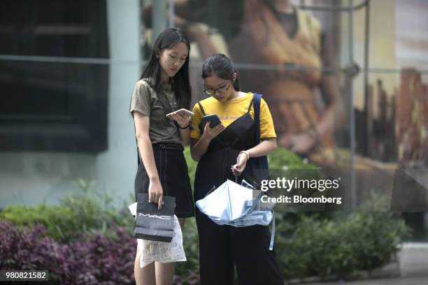 Shoppers look at smartphones outside the CentralWorld shopping mall, operated by Central Pattana Pcl , in Bangkok, Thailand, on Saturday, June 16,...