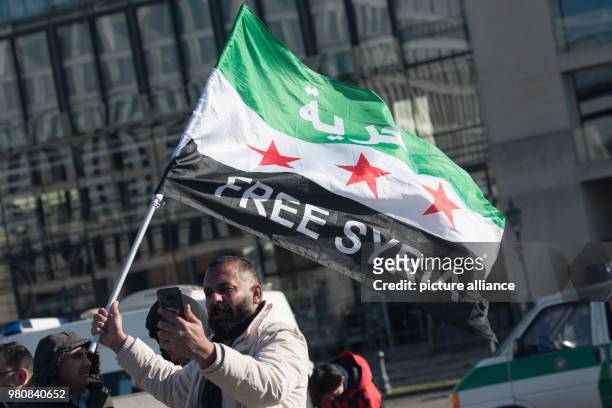 March 2018, Germany, Berlin. A participant of the rally in rememberance of the syrian revolution standing with a syrian flag at Pariser square....