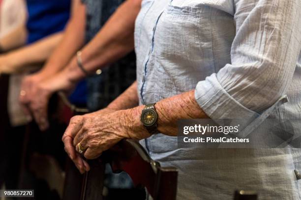 close-up van senior vrouw handen als ze ze rusten op de n voorkant van de stoel van haar in stille gebed - congregation stockfoto's en -beelden