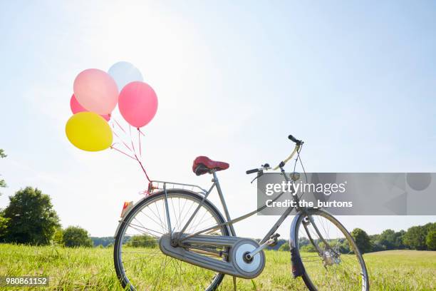 bicycle with colorful balloons on a meadow against sky - verjaardagskado stockfoto's en -beelden