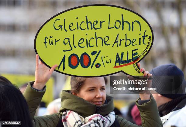 March 2018, Germany, Berlin: A woman holds up a sign reading 'Gleicher Lohn für gleiche Arbeit 100% für alle' . Protestors of the trade union...