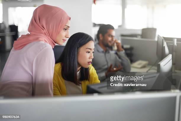 weiblichen kolleginnen und kollegen arbeiten am computer-schreibtisch - multikulturelle gruppe stock-fotos und bilder