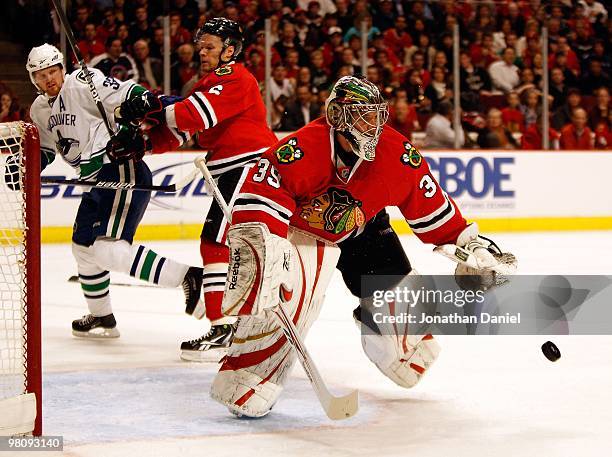 Cristobal Huet of the Chicago Blackhawks keeps his eyes on the puck as teammate Jordan Hendry hits Henrik Sedin of the Vancouver Canucks at the...