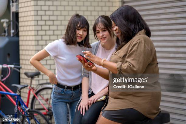 group of friends looking at a smartphone - jgalione stock pictures, royalty-free photos & images