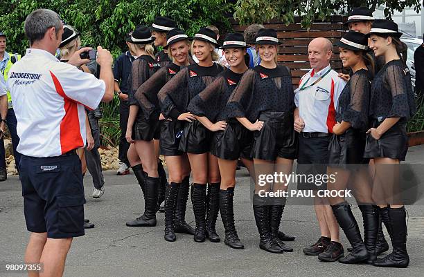 Tyre technician poses with promotional girls as another takes their photo ahead of Formula One's Australian Grand Prix in Melboune on March 28, 2010....