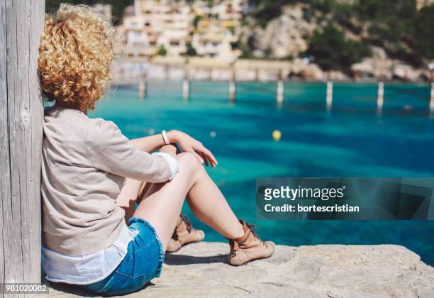 woman sitting by sea - bortes fotografías e imágenes de stock