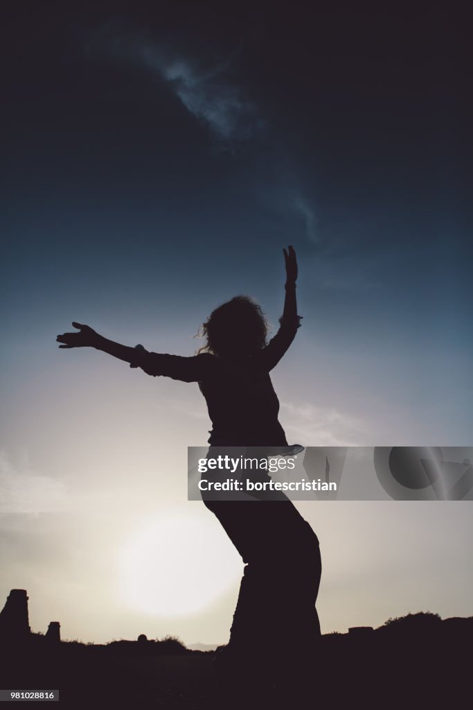 Low Angle View Of Silhouette Woman Dancing Against Sky During Sunset