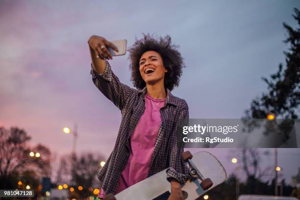 young woman holding skateboard taking a selfie while laughing - extreme skating stock pictures, royalty-free photos & images