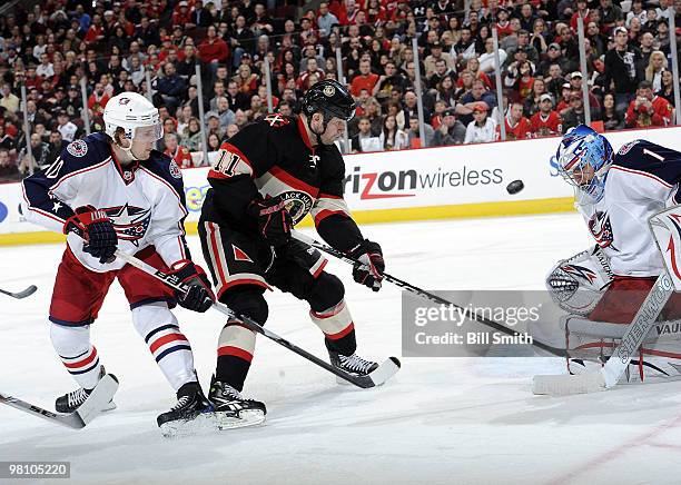 John Madden of the Chicago Blackhawks and Kris Russell of the Columbus Blue Jackets approach goalie Steve Mason of the Jackets, as they chase after...