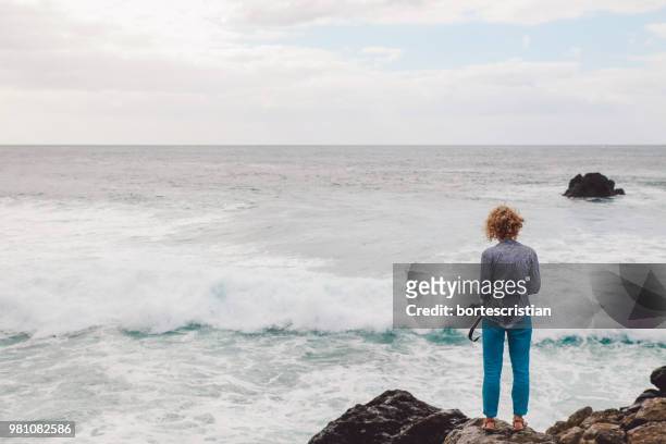 rear view of woman looking at sea against sky - bortes fotografías e imágenes de stock