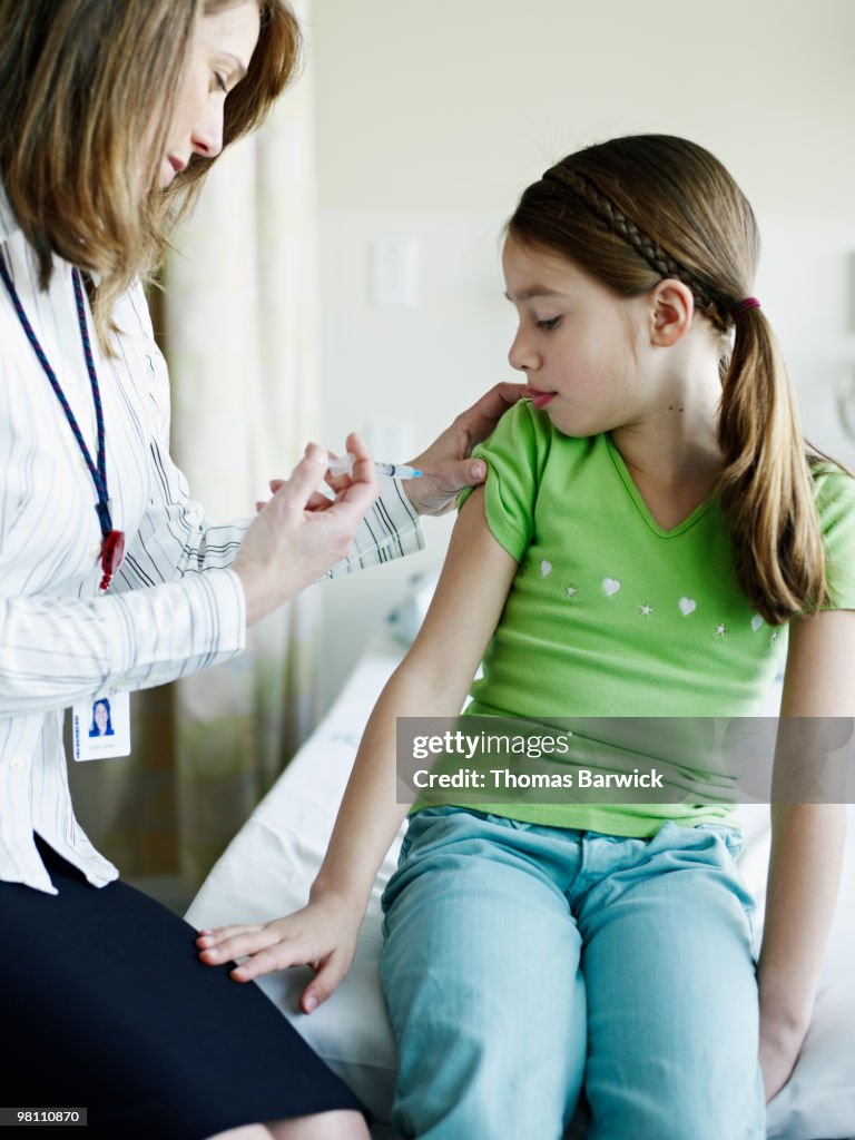 Doctor giving young female patient injection
