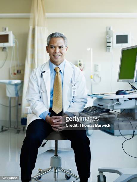 male doctor sitting near computer smiling - doctor sitting stock pictures, royalty-free photos & images