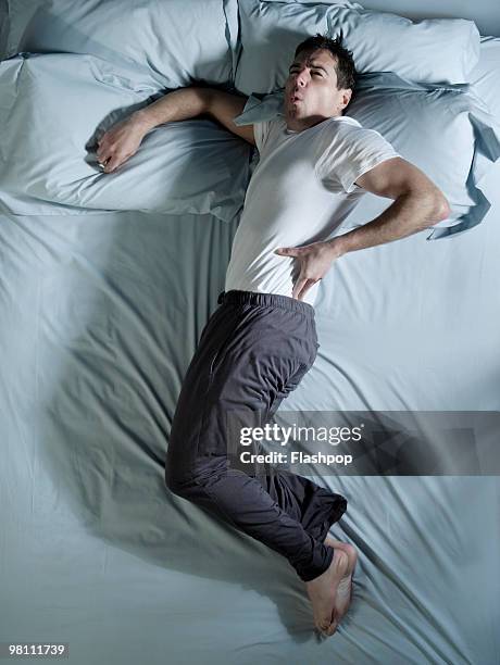 man lying on bed with back pain - acostado de lado fotografías e imágenes de stock