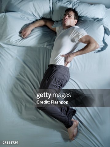 Man lying on bed with back pain Man lying on bed with back pain