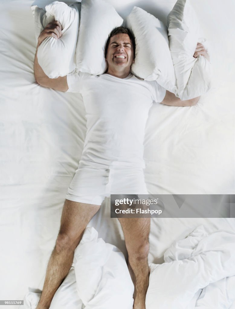 Man in bed using pillows to cover ears