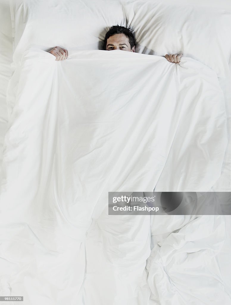 Man peering over the top of bed sheet