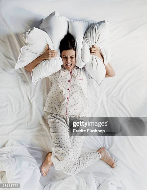 woman in bed using pillows to cover her ears - woman pillow stock pictures, royalty-free photos & images