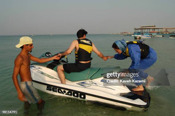 Woman boards a Sea-Doo jet-ski while holding her partner's hand in Kish, a resort island in the Persian Gulf, Iran, 3rd July 2003. She is wearing the...