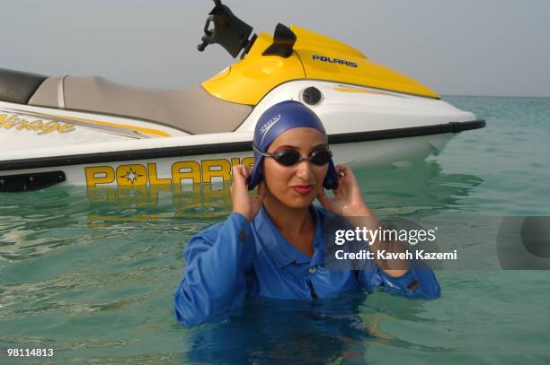 Young woman emerges from the sea after a jet-ski in Kish, a resort island in the Persian Gulf, Iran, 3rd July 2003. She is wearing a swimming cap and...