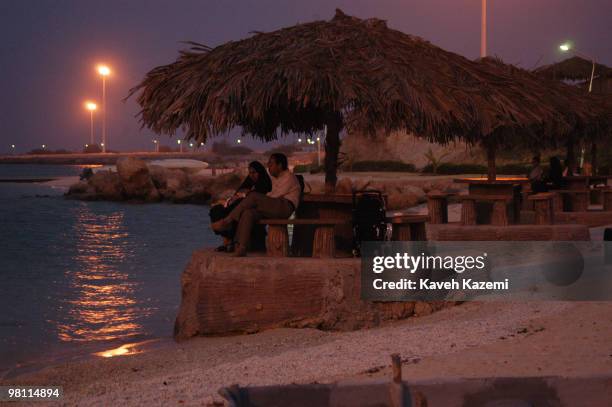 Young couple sit on the beach front with their toddler enjoying the early evening sea breeze in Kish, a resort island in the Persian Gulf, Iran, 4th...