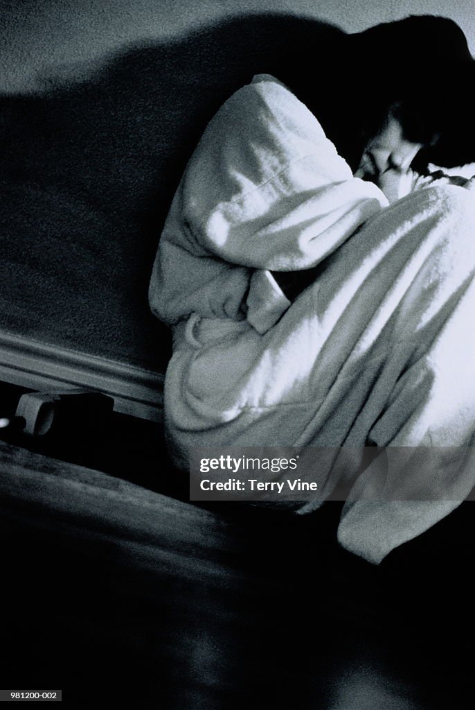 Woman in bathrobe curled on floor looking upset (B&W)