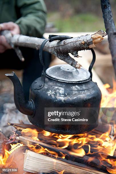 man holding tea kettle over campfire with stick - stick plant part stockfoto's en -beelden