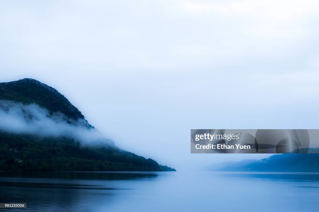 Fog over lake among forest covered hills, Highlands, Scotland, UK