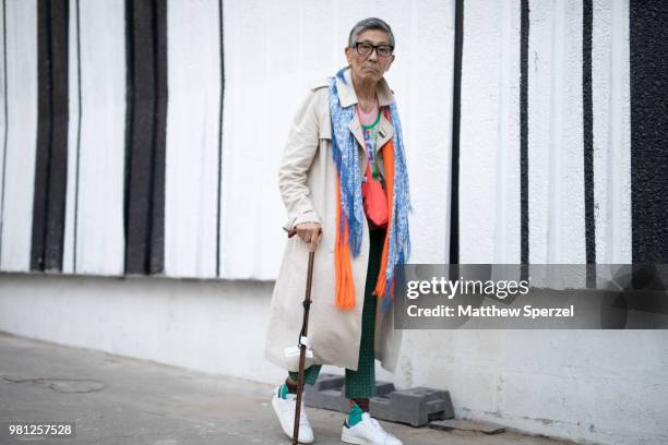 Guest is seen on the street during Paris Men's Fashion Week S/S 2019 wearing a long taupe coat with blue and orange scarf and white sneakers on June...