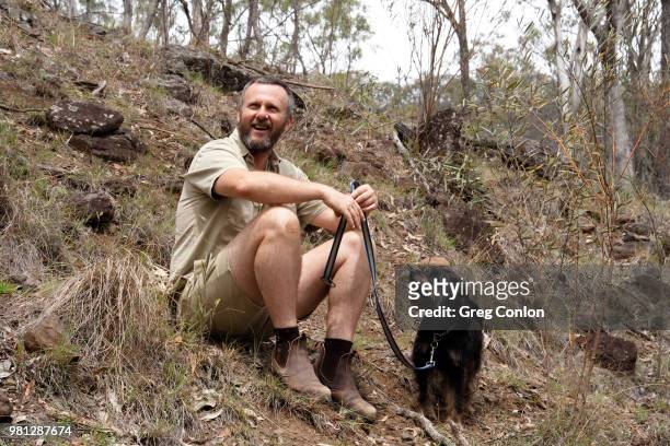 a man and his dog sitting on the side of a hill in the australian bush. - bush dog fotografías e imágenes de stock