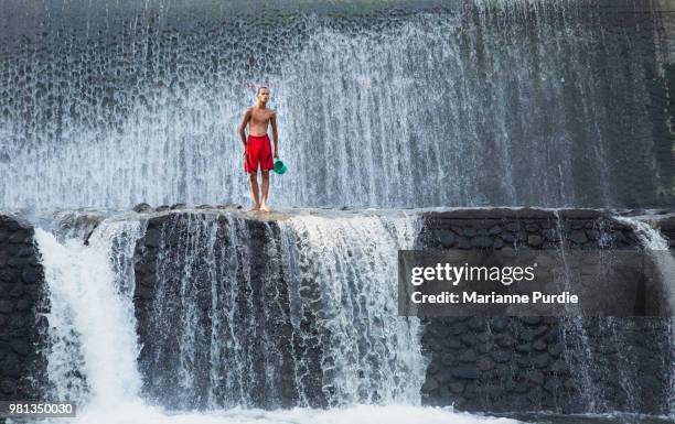 young man standing on weir as water flows over the edges - stuw stockfoto's en -beelden