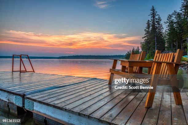 wooden deck chairs on jetty by clear lake at sunrise, riding mountain national park, manitoba, canada - manitoba stock photos et images de collection