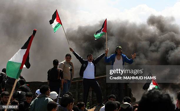 Palestinian youths wave their national flag and set tyres on fire as they clash with Israeli soldiers at the border fence near Gaza City on March 30,...