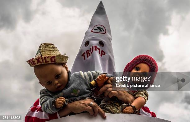 June 2018, Mexico, Mexico City: A man dressed up a a Ki-Klux-Klan member holds two puppets during a protest against the migration policies of USA....