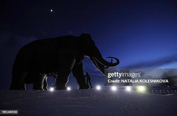 Man climbs a bronze sculpture of a mammoth in the western Siberian city of Khanty-Mansiysk on March 24, 2010. AFP PHOTO/NATALIA KOLESNIKOVA