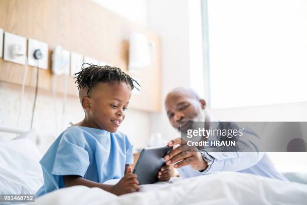 man showing digital tablet to sick grandson on bed - hospital visit stock pictures, royalty-free photos & images