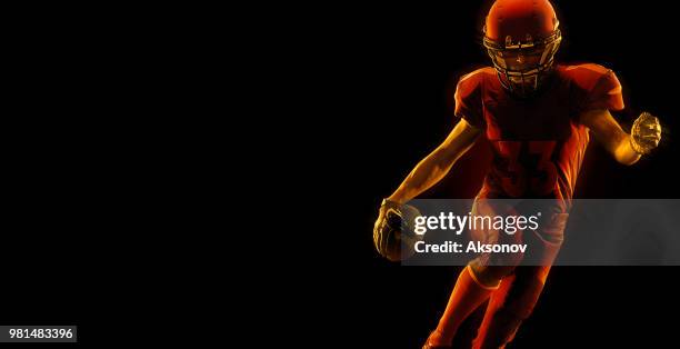 us-amerikanischer american-football-spieler mit ball auf einem dunkelroten hintergrund - phosphorescence stock-fotos und bilder