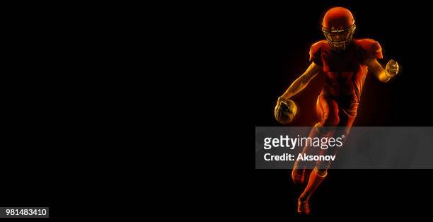 us-amerikanischer american-football-spieler mit ball auf einem dunkelroten hintergrund - phosphorescence stock-fotos und bilder