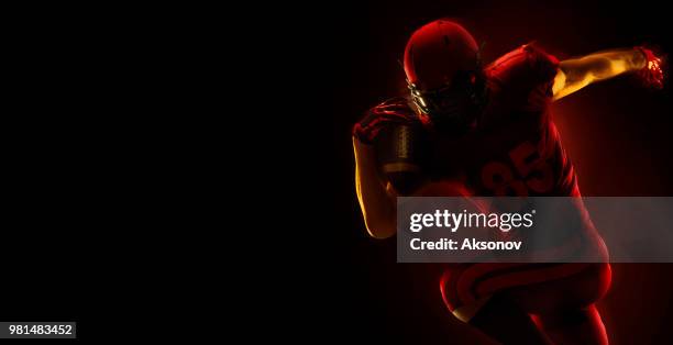 us-amerikanischer american-football-spieler mit ball auf einem dunkelroten hintergrund - phosphorescence stock-fotos und bilder