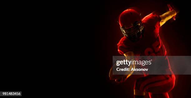 us-amerikanischer american-football-spieler mit ball auf einem dunkelroten hintergrund - phosphorescence stock-fotos und bilder