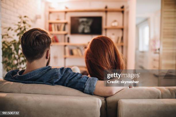 rear view of loving couple watching tv at home. - couple on sofa stock pictures, royalty-free photos & images