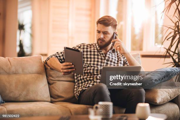 jeune homme multi-tâches utilisant la technologie sans fil dans le salon. - multi tasking photos et images de collection