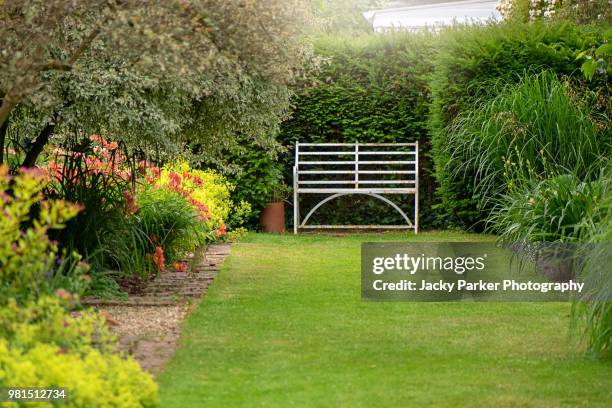 an english summer garden with a wrought iron white seat - flouté photos et images de collection