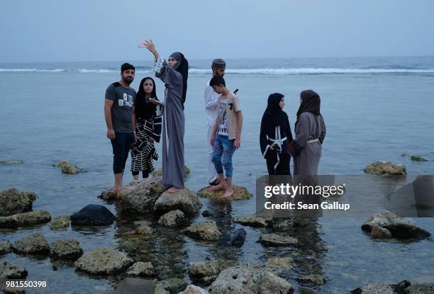 Teenagers, including girls wearing abayas that break markedly from the traditional black, shoot selfies as they step among stones in the water of the...