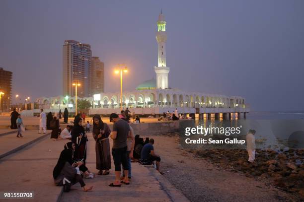 People relax on a Friday evening along the Corniche waterfront as the Al Rahma mosque stands behind on June 22, 2018 in Jeddah, Saudi Arabia. The...