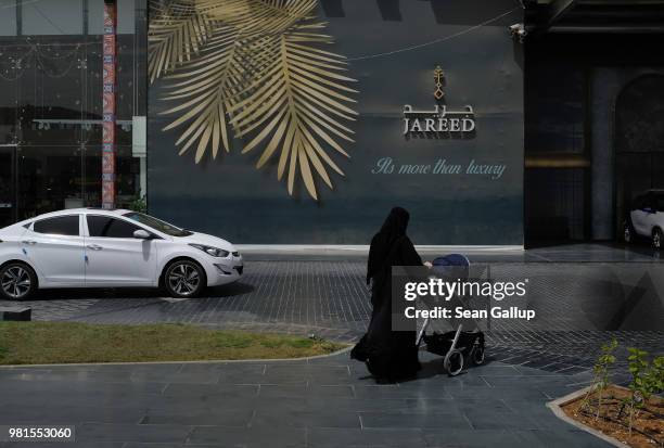 Woman wearing a traditional niqab and black abaya pushes a child stroller outside an upscale shopping center on June 20, 2018 in Riyadh, Saudi...