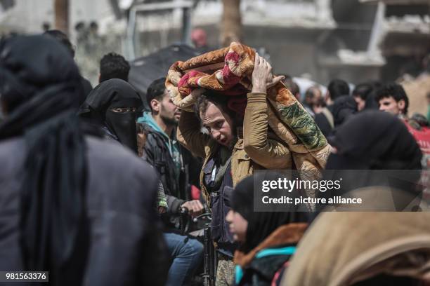 Syrian man carries an AK-47 assault rifle and a personal item wrapped in a blanket while being evacuated from Zamlka in Syria's eastern Al-Ghouta...