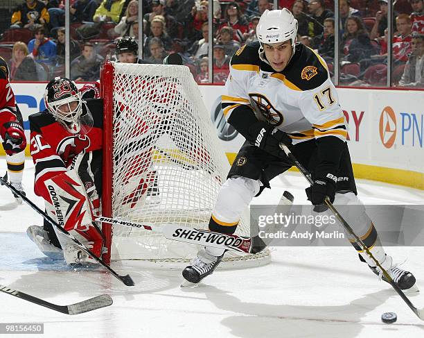 Milan Lucic of the Boston Bruins plays the puck behind the net while being stick checked by goaltender Martin Brodeur of the New Jersey Devils during...