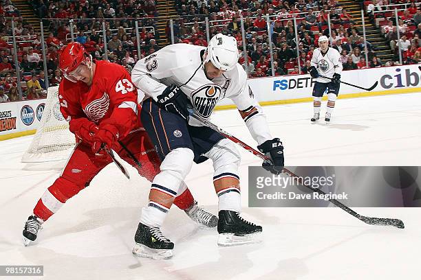 Jason Strudwick of the Edmonton Oilers and Darren Helm of the Detroit Red Wings search for the loose puck during an NHL game at Joe Louis Arena on...