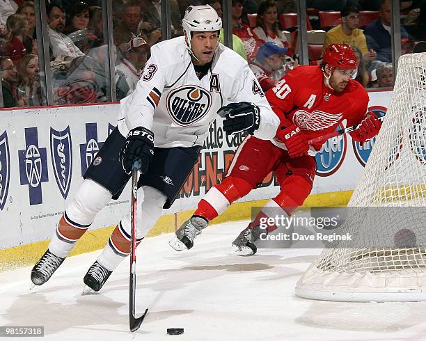 Jason Strudwick of the Edmonton Oilers skates with the puck behind the net as Henrik Zetterberg of the Detroit Red Wings follows during an NHL game...