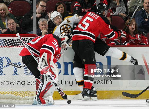 Patrice Bergeron of the Boston Bruins is checked hard into the boards by Colin White of the New Jersey Devils as Martin Brodeur makes a save during...